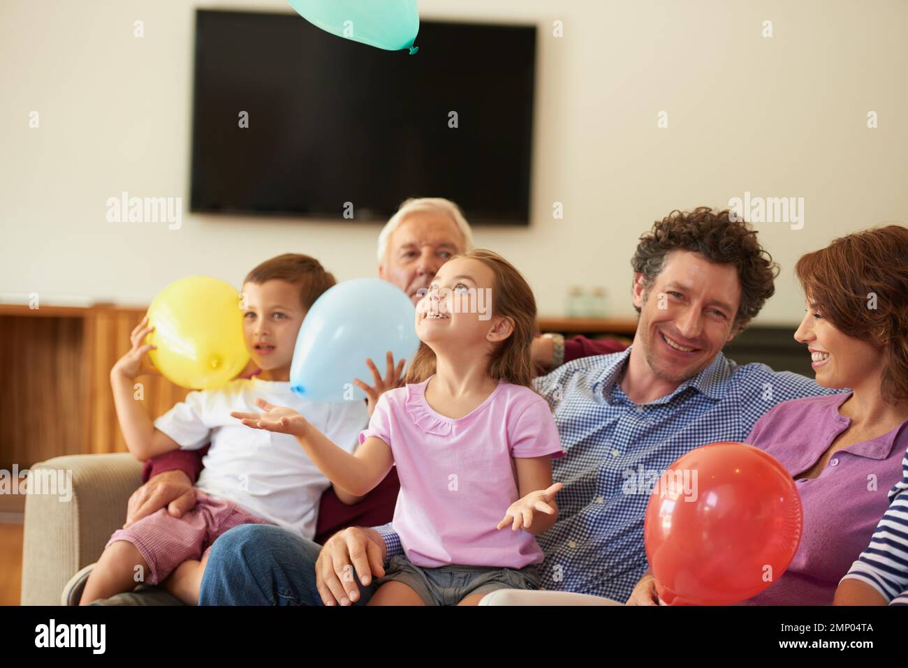 Every childs favorite. a brother and sister playing with balloons while sitting with their family. Stock Photo