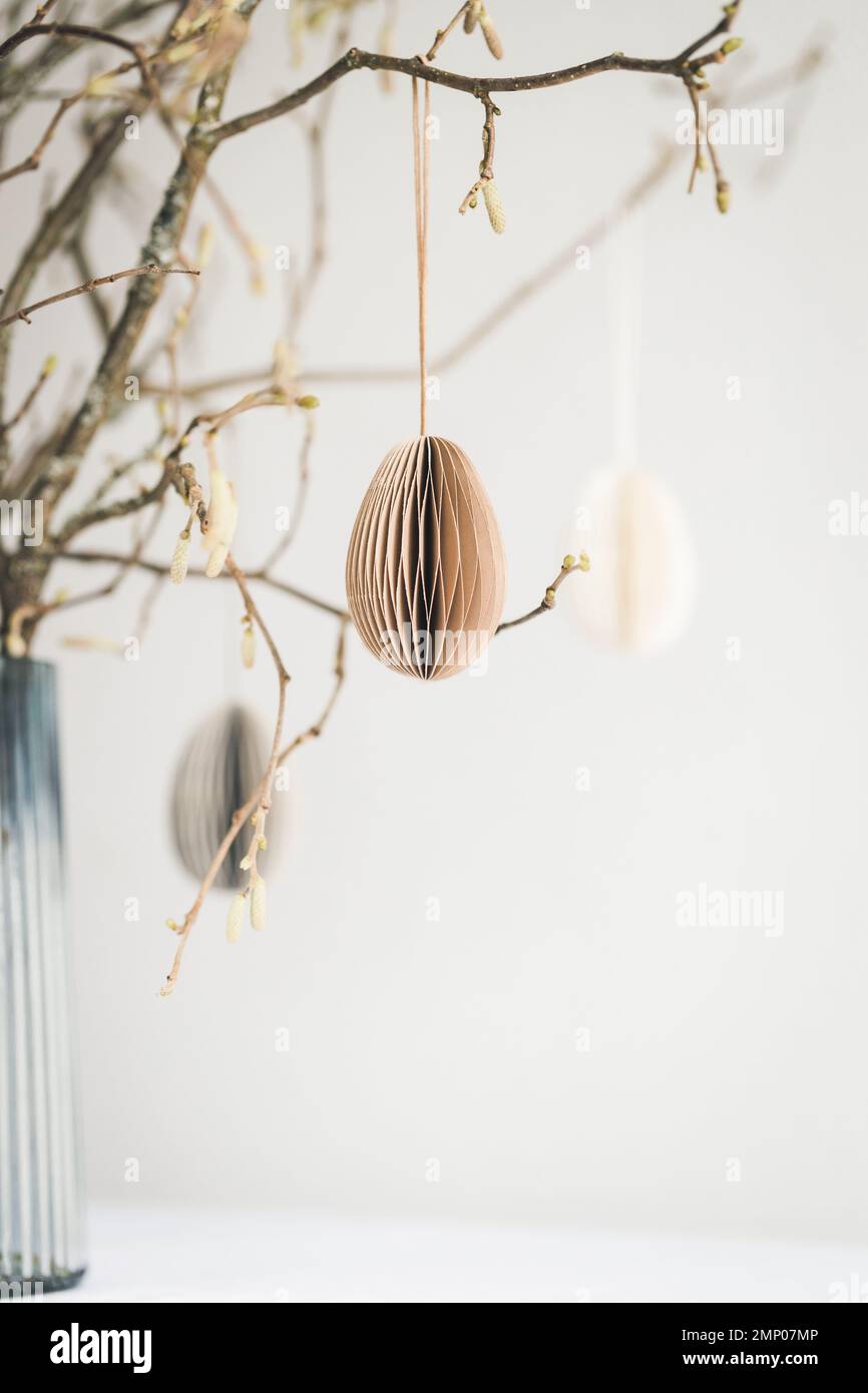 Easter paper eggs hanging on branches against white wall. Stock Photo