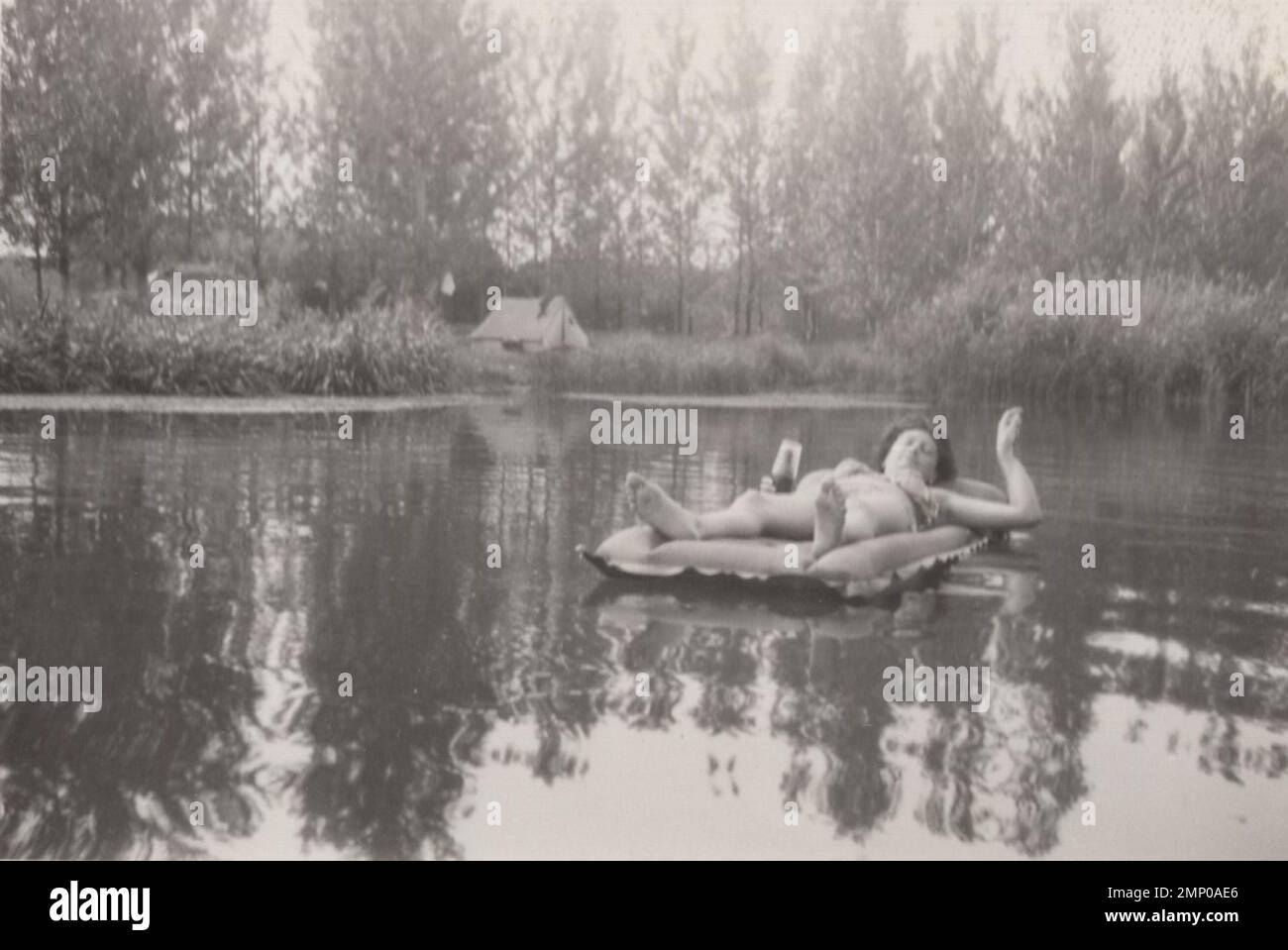 vintage moment / vintage funny moment / vintage photograph / power of the moment / magic moments /enjoy your life photo,lady smoking a cigarette and drinking beer while she is sunbathing and lying Swimming pool Mattress at summer time at 1940s. Stock Photo