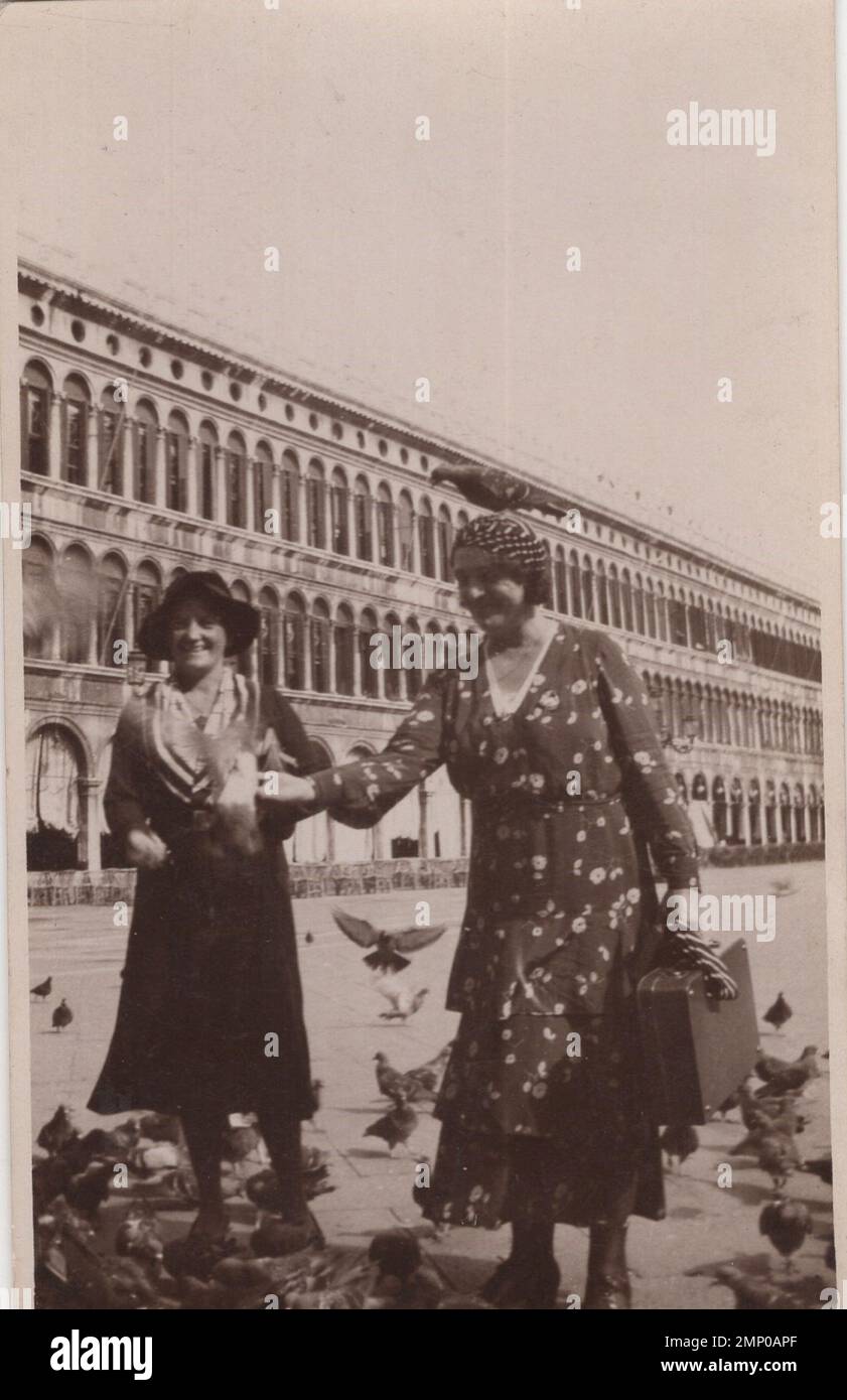 vintage moment / vintage funny moment / vintage photograph / power of the moment / magic moments / happy ladies are feeding pigeons on a big squareat the 1920s. maybe it is Italy? not a single dove on the picture. / well dressed ladies / pigeon is standing on the lady's head. Stock Photo