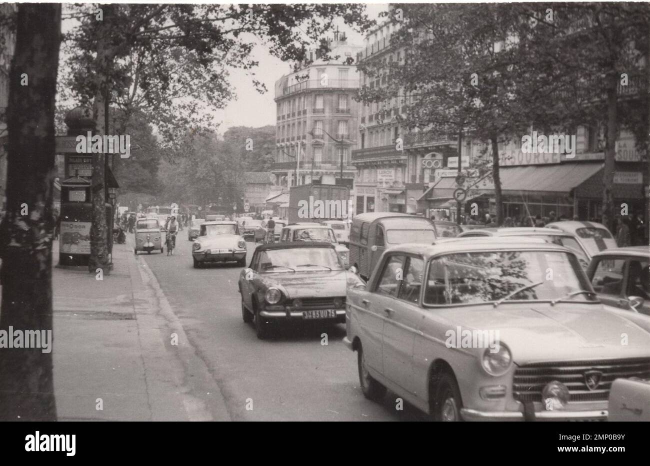 vintage moment / vintage funny moment / vintage photograph / power of the moment / magic moments / vintage street view possibly from France at the 1960's- there are lots of french cars bicycle and tuc tuc. it was  a busy day possibly a monday :) Stock Photo
