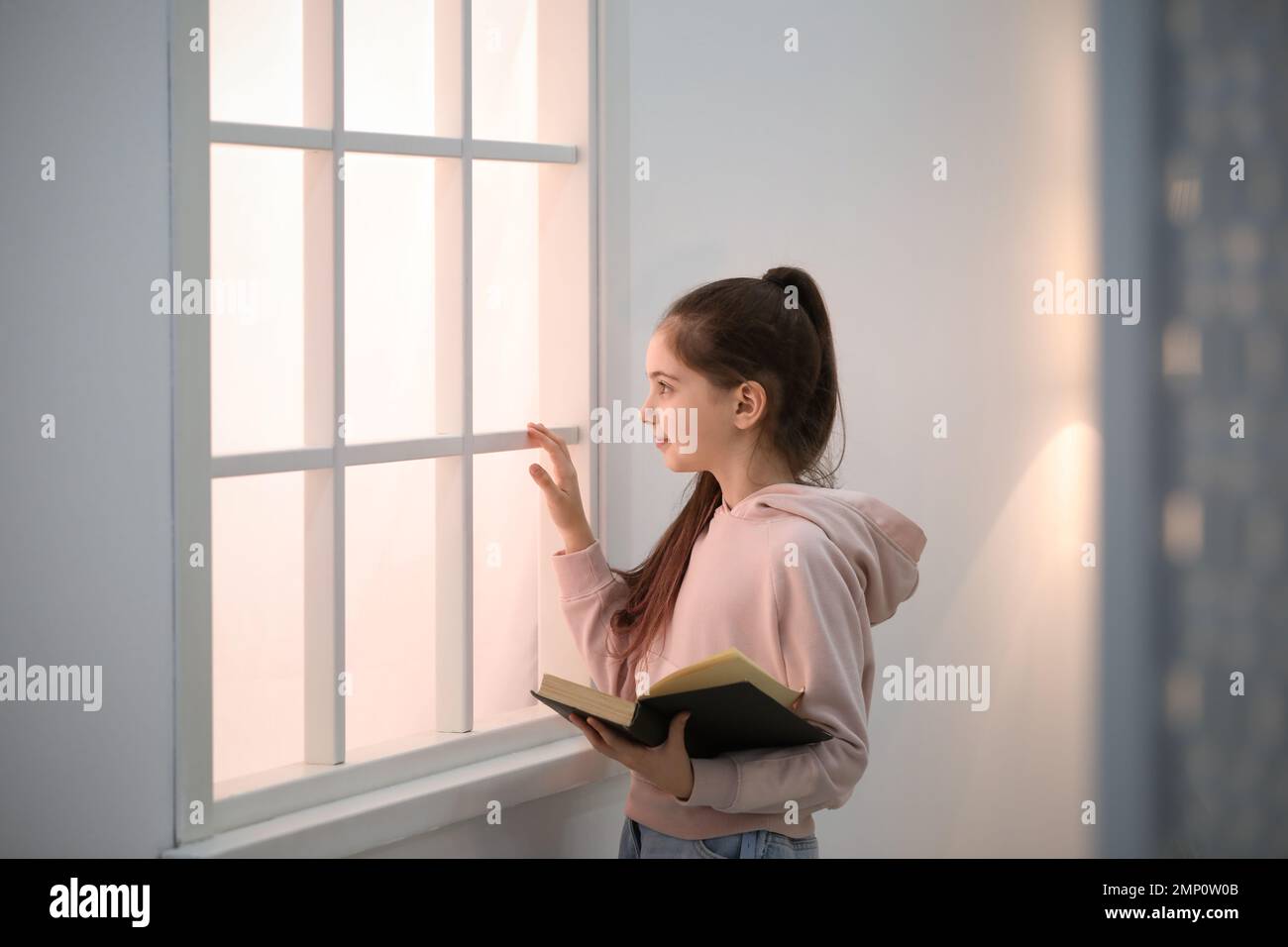 Cute little girl reading book near window at home Stock Photo - Alamy