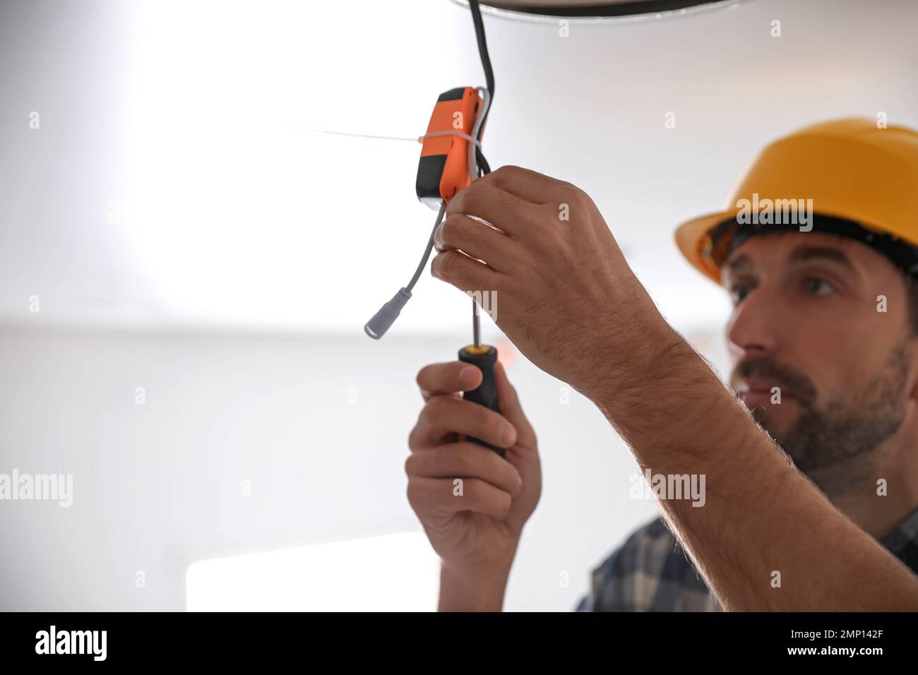 Worker repairing lamp on stretch ceiling indoors. Space for text Stock Photo