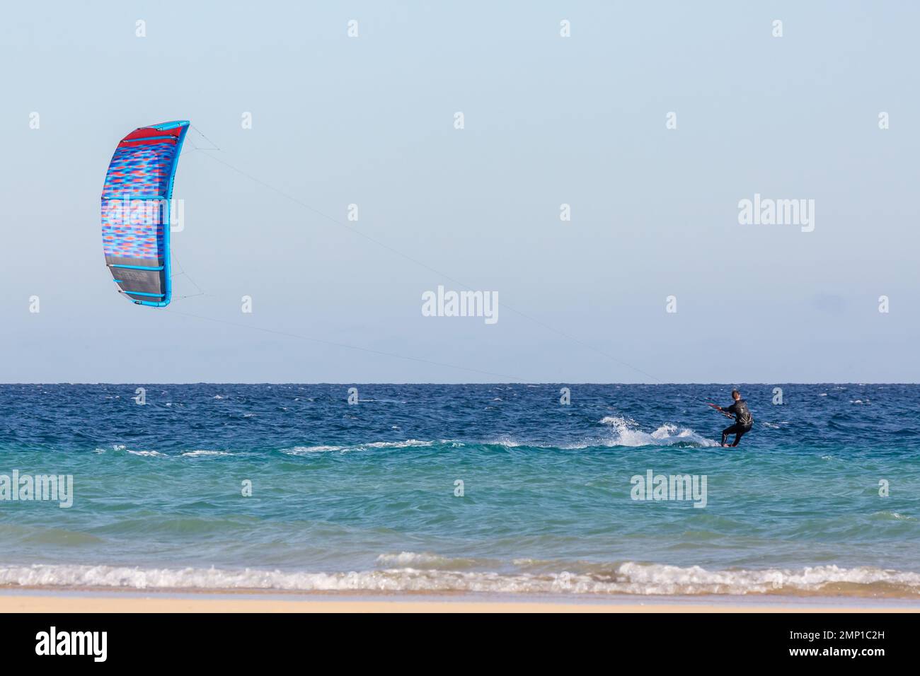 Kitesurfer sliding on the water carried away by his blue kite. Sotavento Beach, Furteventura, Canary Islands. Stock Photo