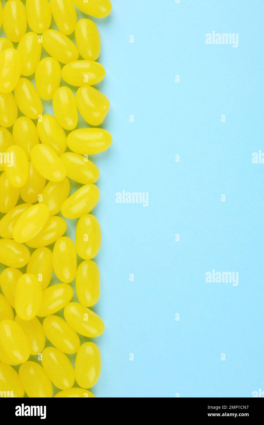 Many delicious lemon jelly beans on light blue background, flat lay