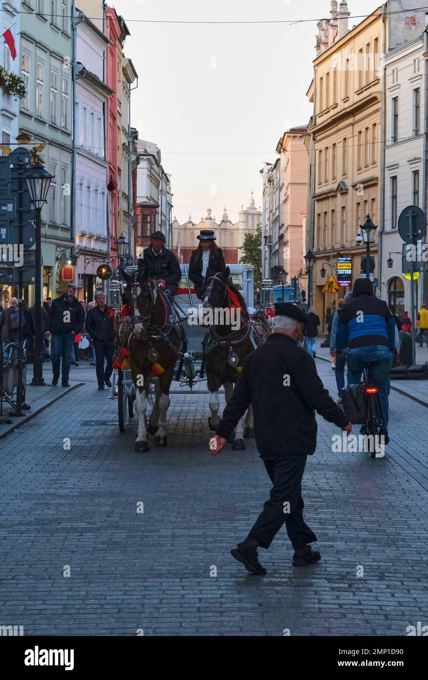An old person crossing the street in Krakow with a horse carriage in the background. Stock Photo
