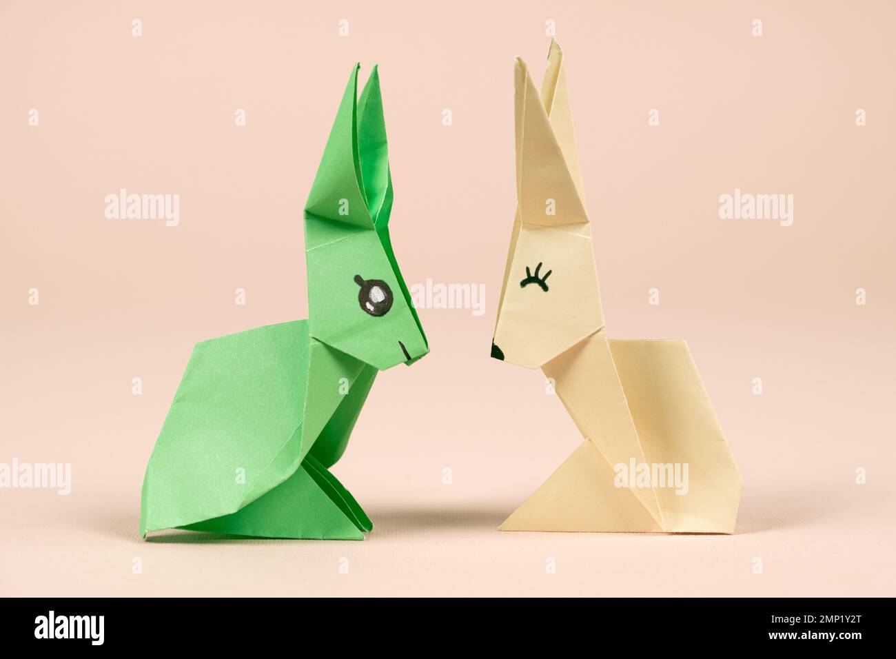 A green and yellow origami rabbits on a beige background. Crafts for Easter, fold from paper, do it yourself Stock Photo
