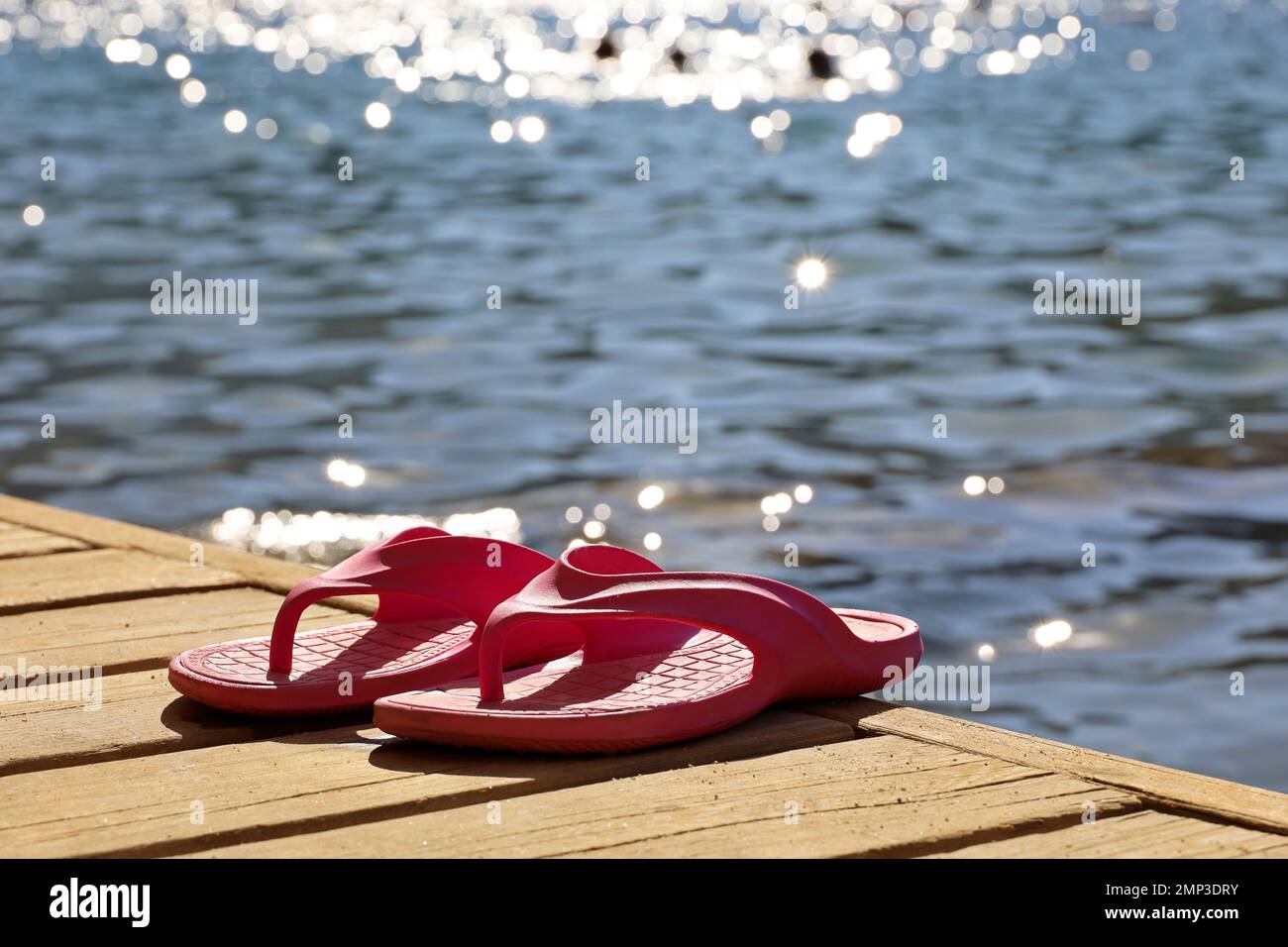 Holidays on a beach, pink female flip-flops on wooden boards on background of shining sea waves and swimming people Stock Photo