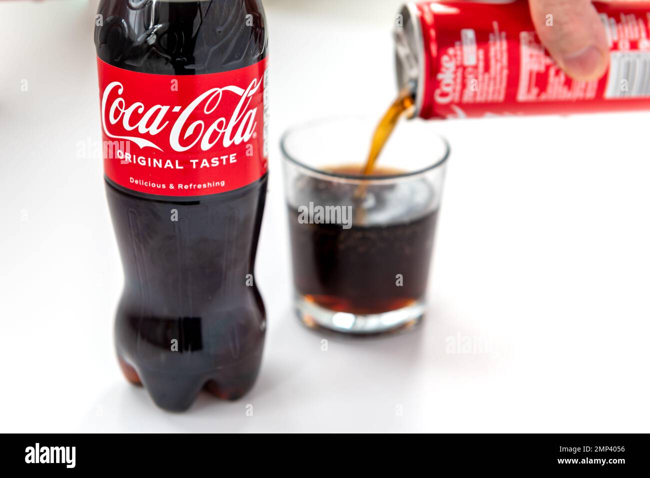 London. UK- 01.29.2023. A bottle of Coca Cola original taste isolated in white with a person pouring a can of the drink into a glass. Stock Photo