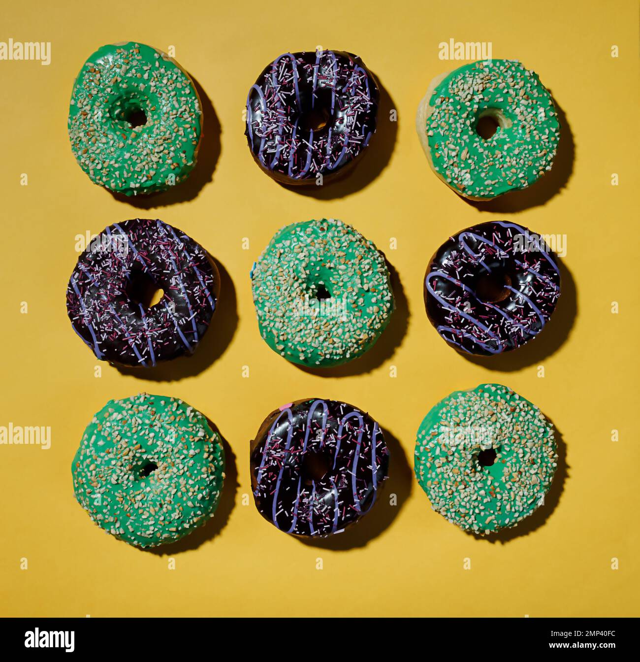 Multicolored donuts pattern on yellow background. Hard shadows. Flat lay. Top view Stock Photo