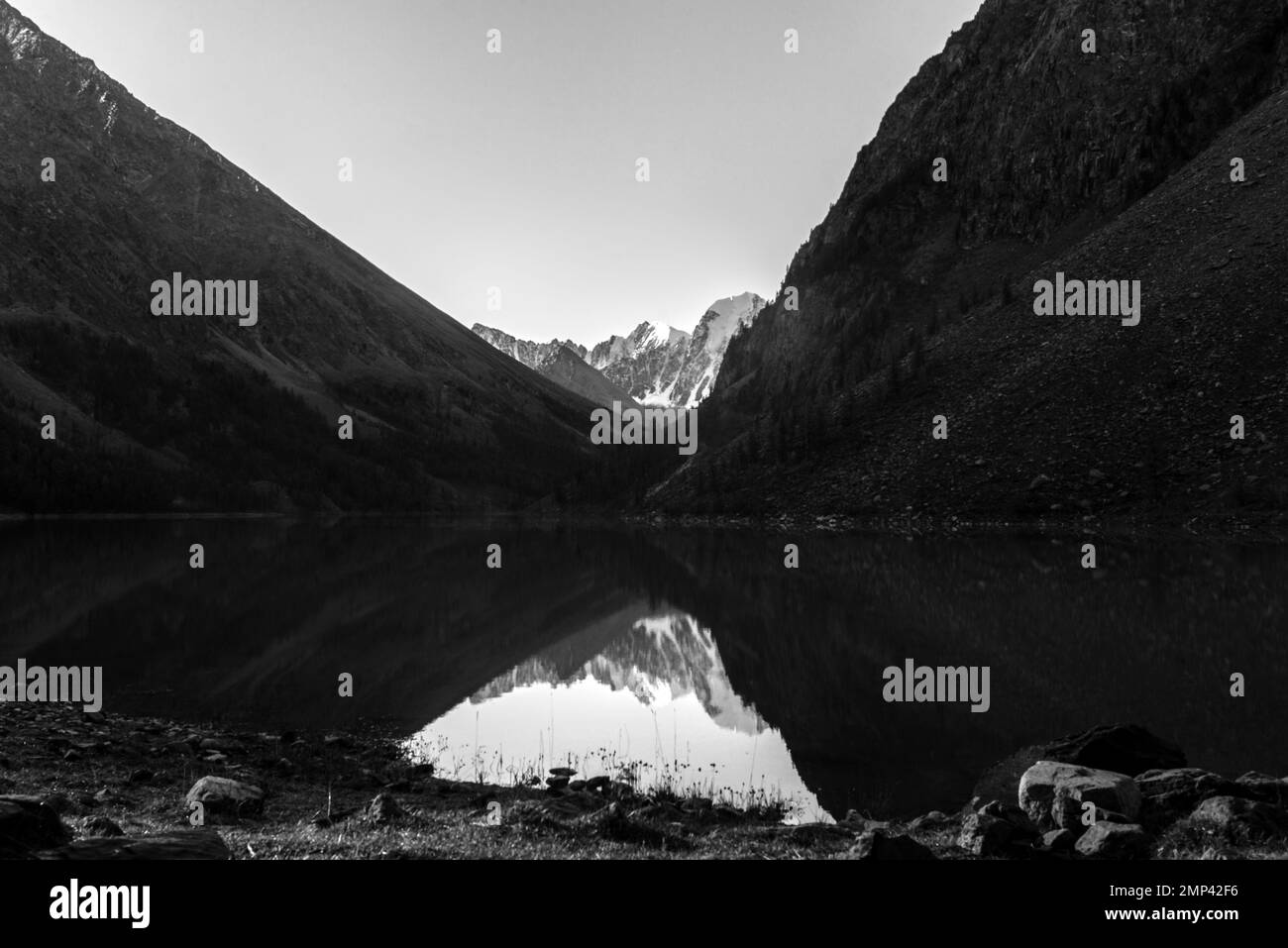 Black and white photo of a lake among mountains with reflection of peaks with glaciers and snow in Altai. Stock Photo