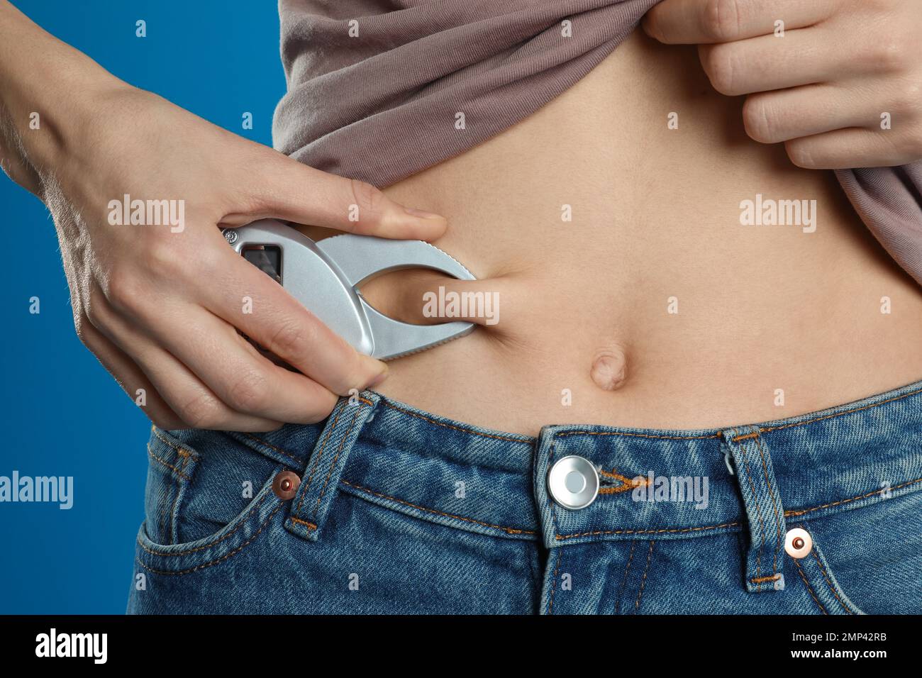 https://c8.alamy.com/comp/2MP42RB/young-woman-measuring-body-fat-with-caliper-on-blue-background-closeup-2MP42RB.jpg
