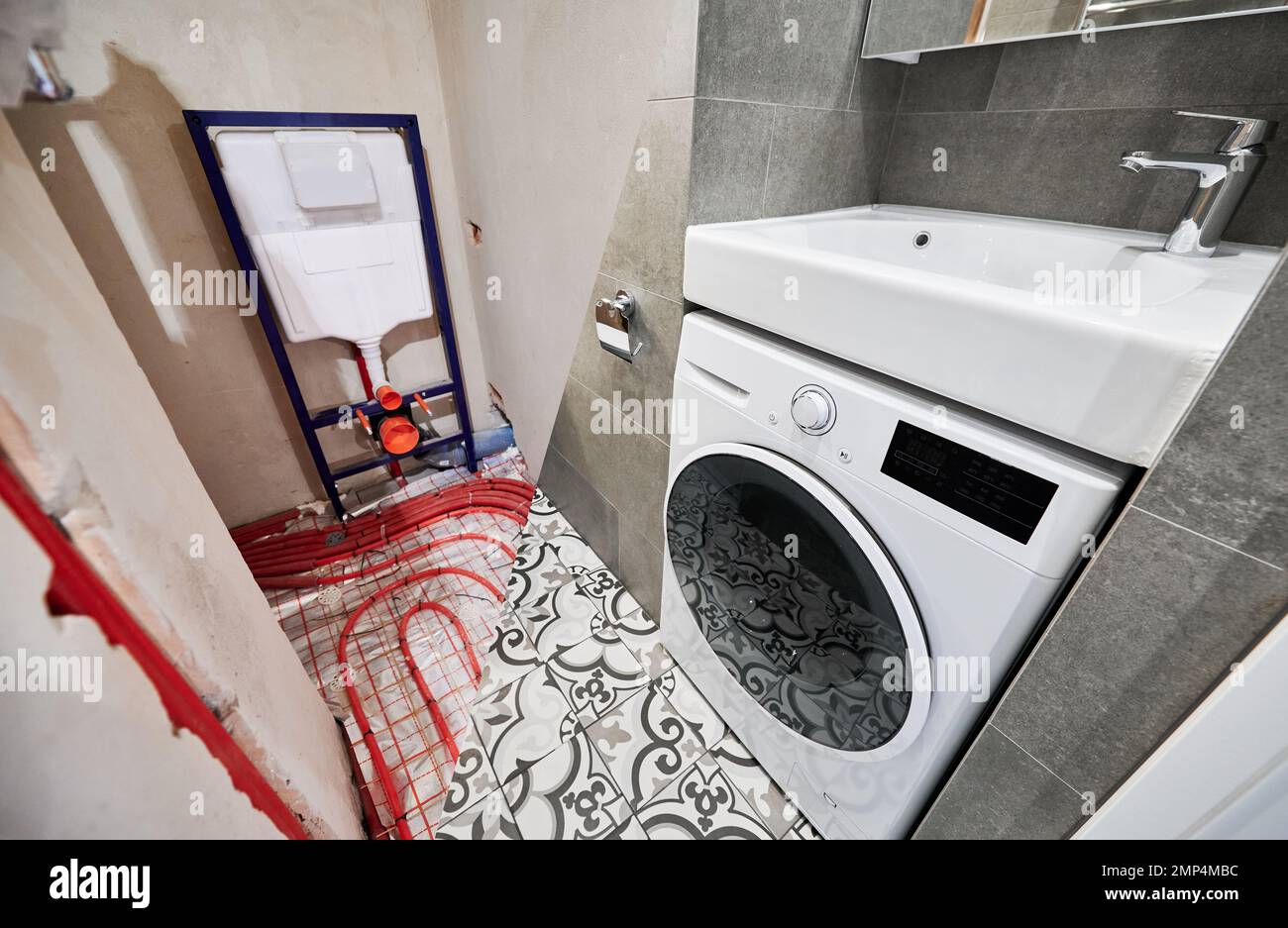 Comparison of washroom lavatory before and after renovation. Old apartment restroom with underfloor heating pipes and new renovated toilet room with washing machine and washbasin. Stock Photo
