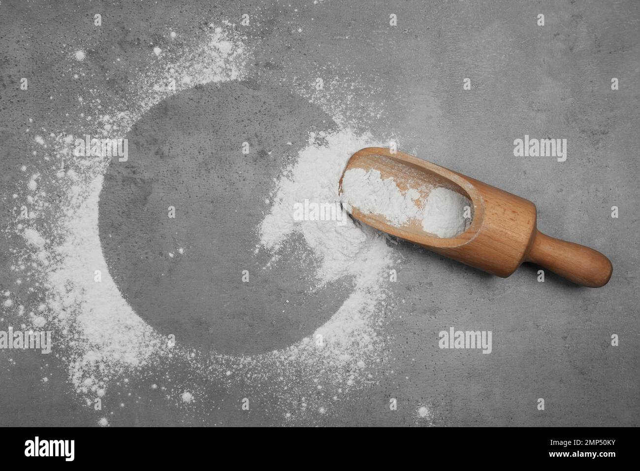 Flour and wooden scoop on light grey table, top view. Space for text