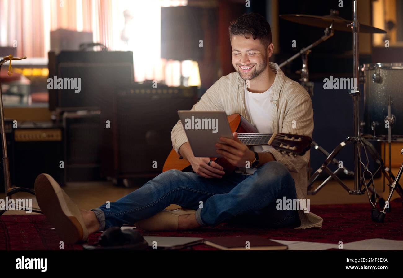 Digital tablet, guitar and man in a recording studio for music production or acoustic performance. Musician, artist and happy male guitarist on a Stock Photo