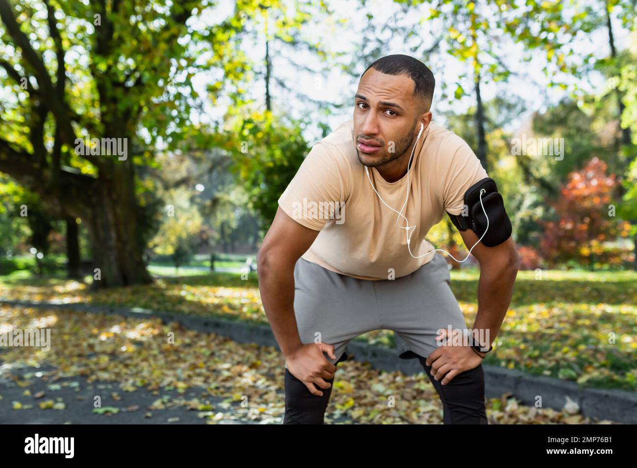 Young African American male athlete resting after jogging, listening to music in headphones. Tiredly looking at the camera. Stock Photo