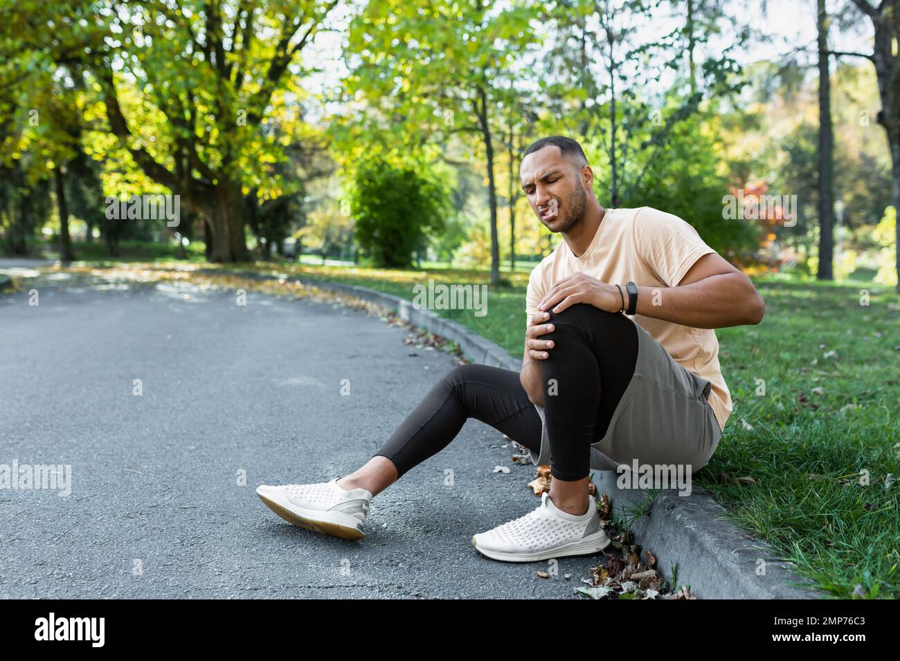 Young African American male athlete sitting in the park on a treadmill, holding his knee