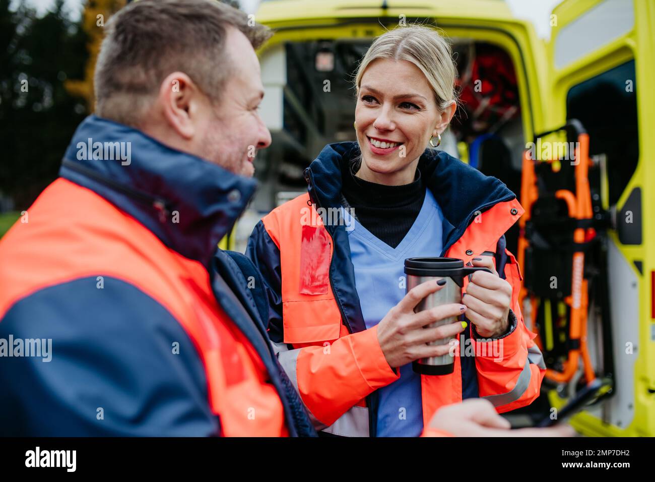 Rescuers having break in front of ambulance car, talking and drinking coffee. Stock Photo