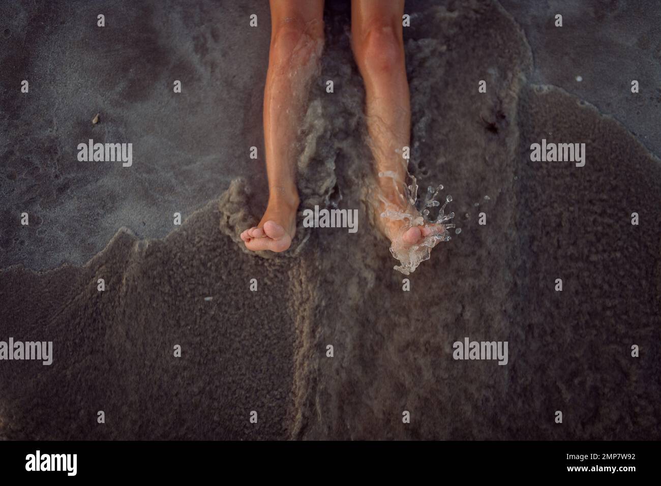 High angle view of childs legs in the sea. Stock Photo