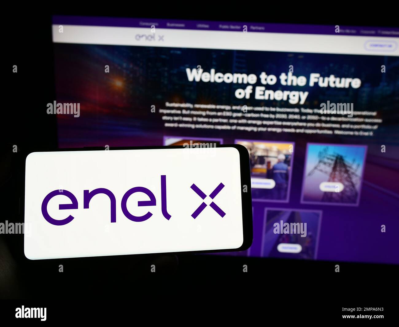 Person holding smartphone with logo of Italian energy company Enel X on screen in front of website. Focus on phone display. Stock Photo