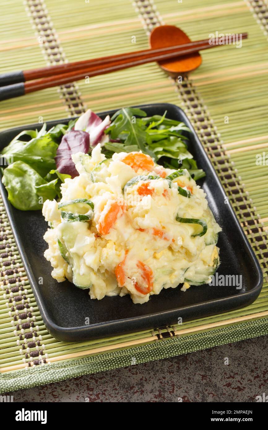 Japanese potato salad with carrots, eggs and fresh cucumber close-up in a plate on the table. Vertical Stock Photo