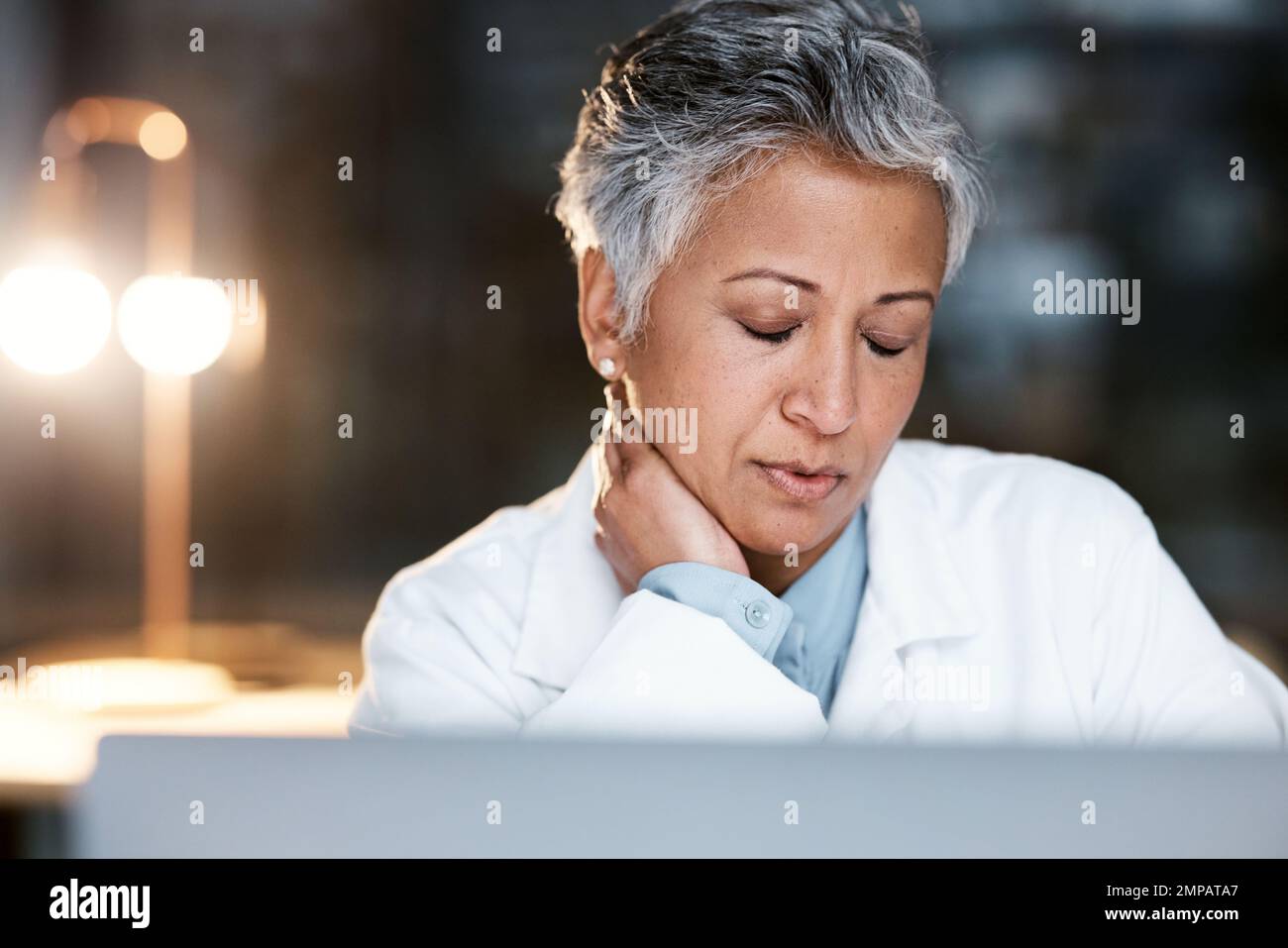 Night, neck pain and burnout with doctor at laptop for medical, thinking and deadline review. Stress, accountability and mental health with senior Stock Photo