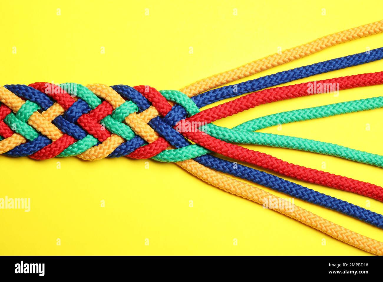 Braided colorful ropes on yellow background, top view. Unity concept ...