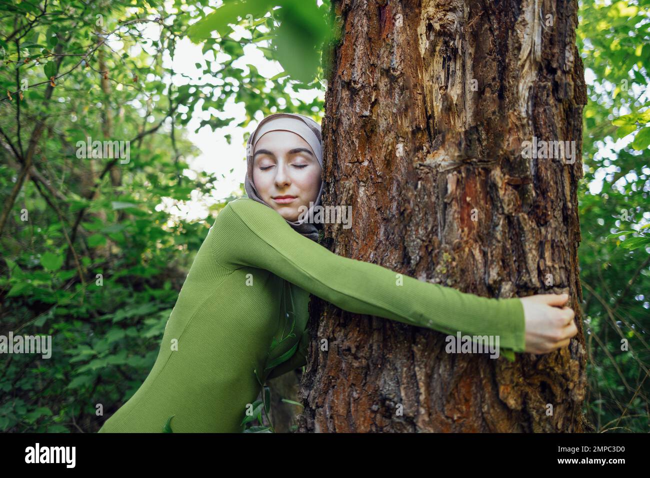 Muslim teen girl hugging a tree. Close up portrait of a young female in a hijab and casual clothes in the park. Protecting the environment and caring Stock Photo