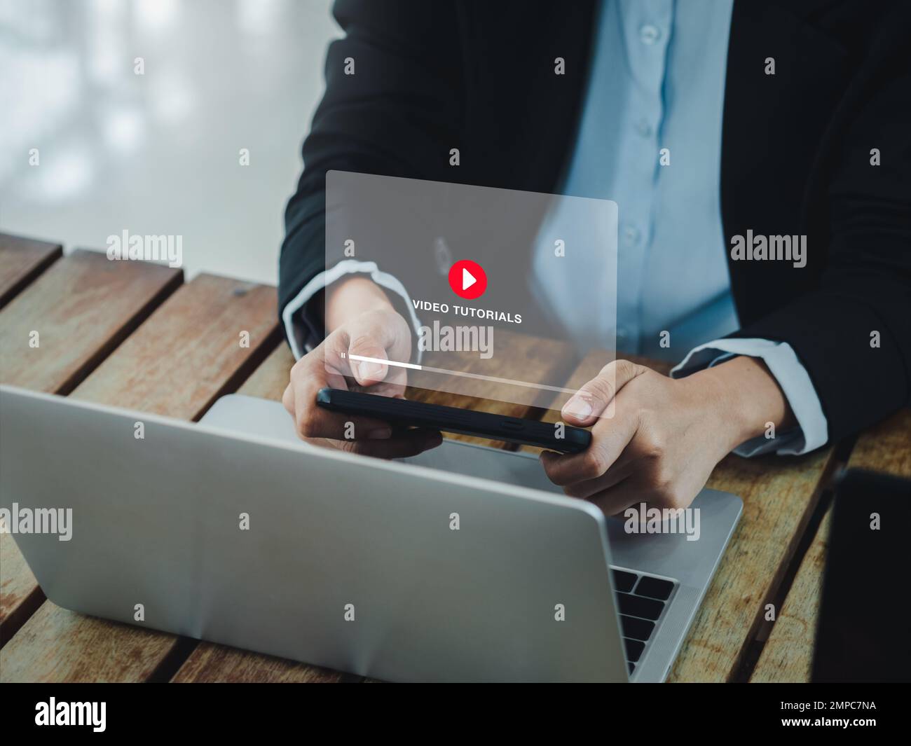 Online video tutorial concept. Red play icon on video tutorial virtual screen display on mobile smartphone while using laptop computer, watching by bu Stock Photo