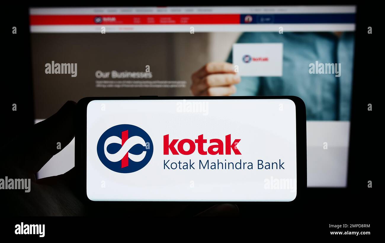 Person holding smartphone with logo of Indian financial company Kotak Mahindra Bank on screen in front of website. Focus on phone display. Stock Photo