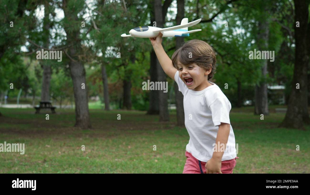 One happy child running outside with plane glider toy. Kid throwing airplane at park Stock Photo