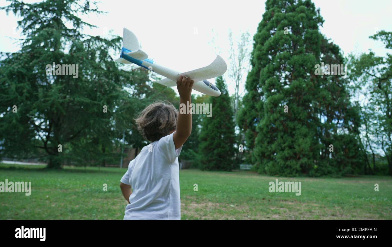 Carefree child running outdoors holding airplane glider. Kid throwing toy plane at park Stock Photo