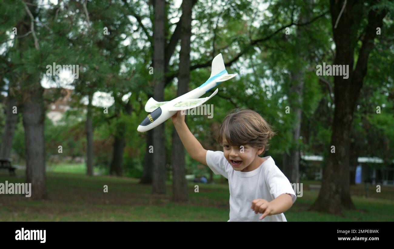 One happy child running outside with plane glider toy. Kid throwing airplane at park Stock Photo