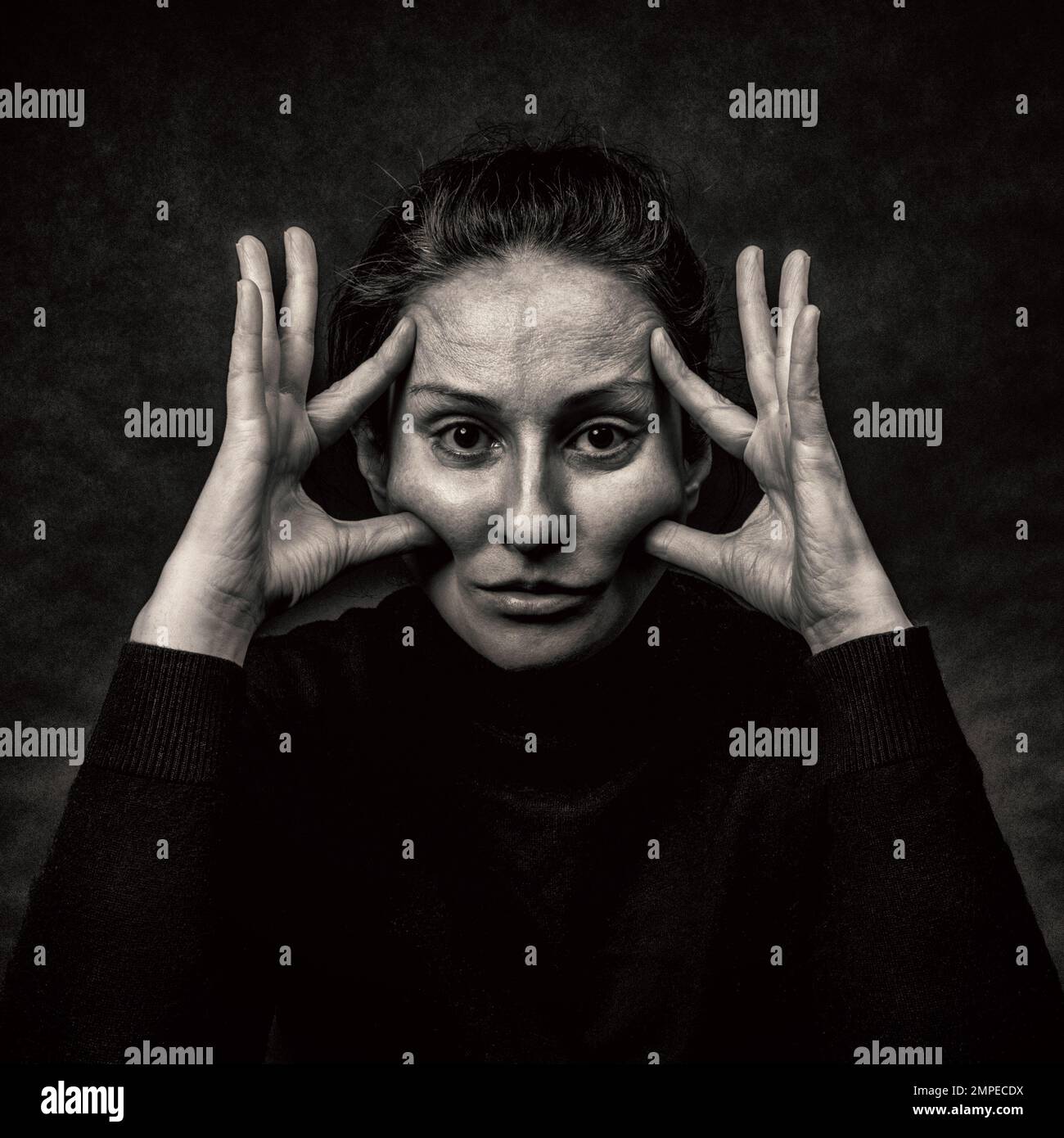 Conceptual dark portrait of woman stretching the skin of her face.  Problems with skin, wrinkles, imperfections, demonstration against plastic surgery Stock Photo