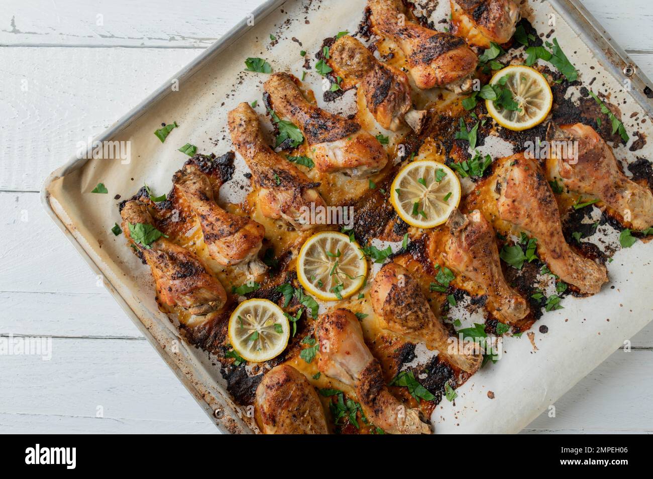 Oven roasted harissa chicken drumsticks on a baking sheet with herbs and lemon isolated on white