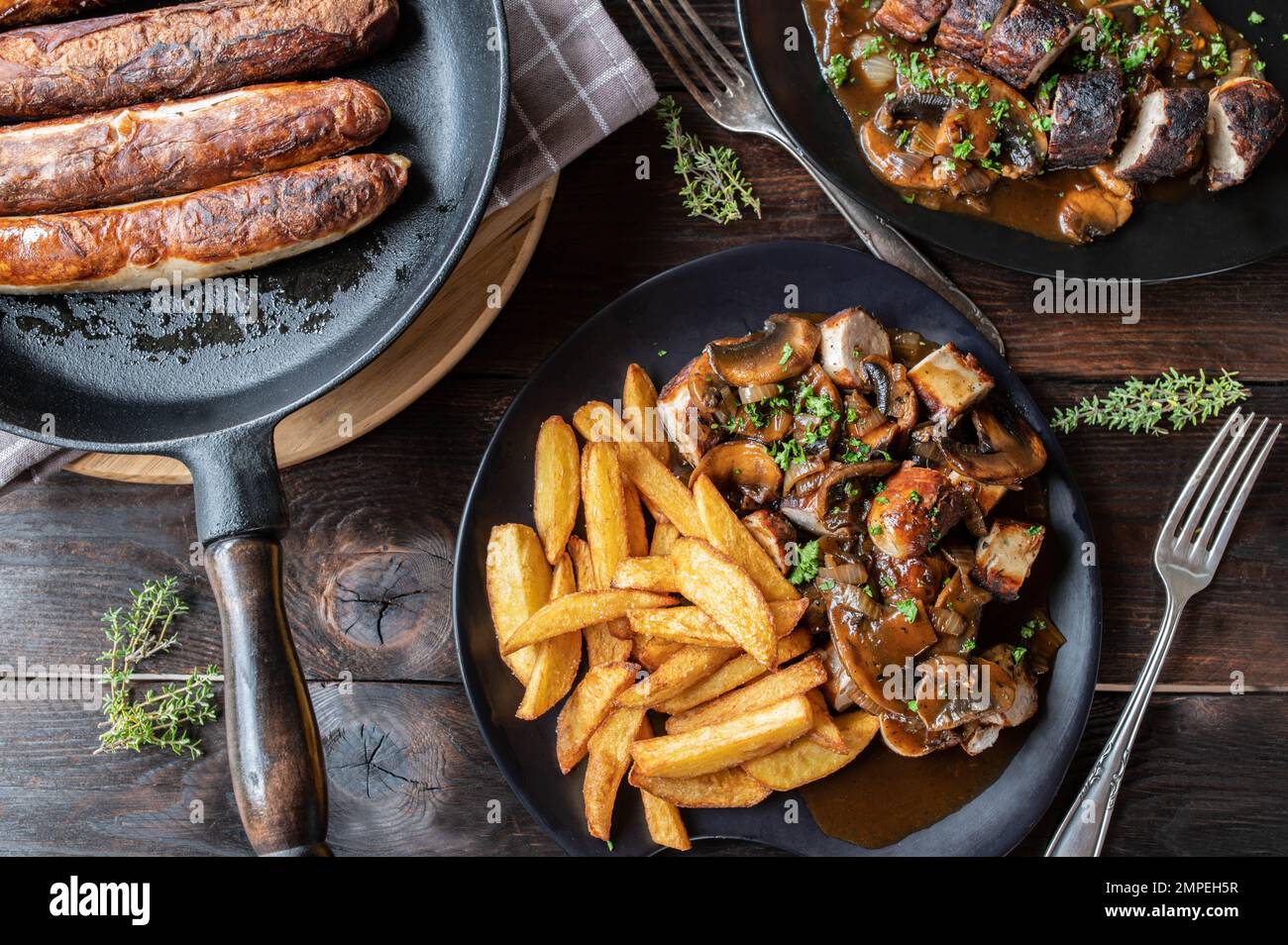 Bratwurst meal with onion, mushroom sauce and french fries on wooden table. Flat lay Stock Photo