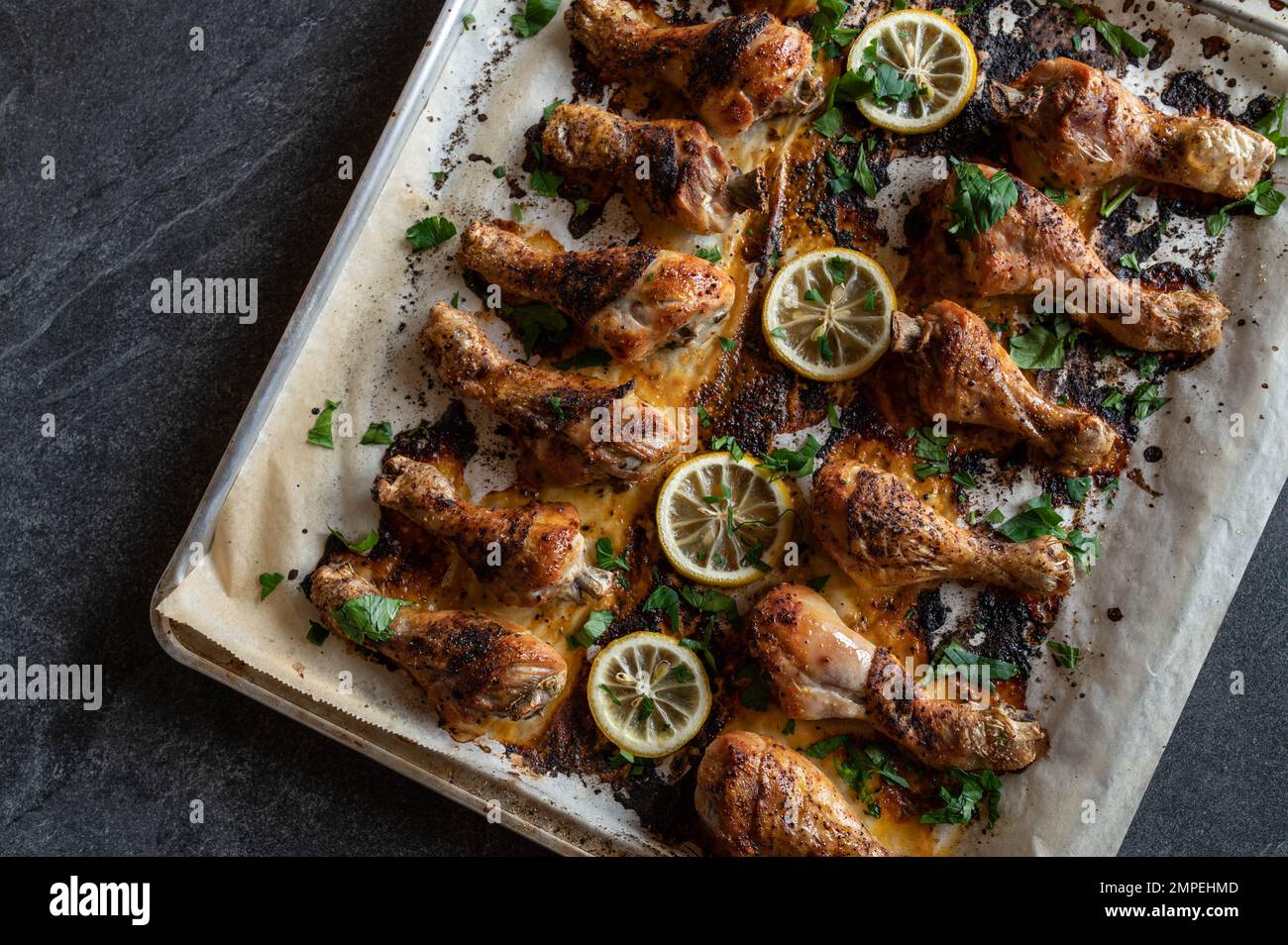 Oven baked chicken drumsticks on a baking tray isolated on dark background. Flat lay Stock Photo