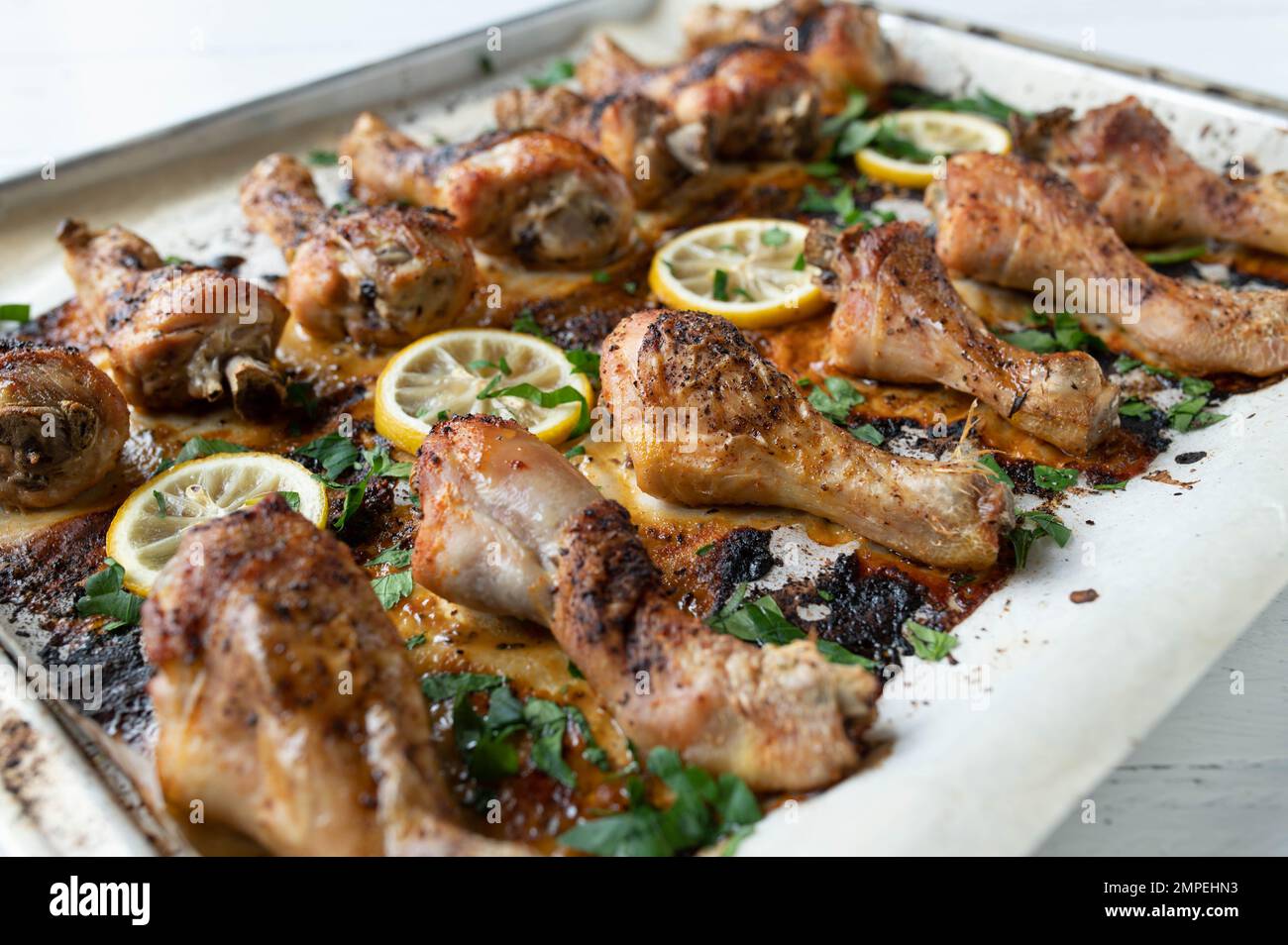 Chicken drumsticks oven baked with lemon and herbs on a baking sheet Stock Photo