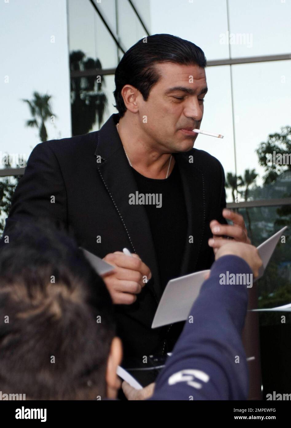 Actor Tamer Hassan smokes a cigarette as he signs autographs at the
