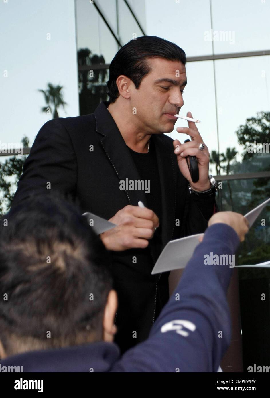 Actor Tamer Hassan smokes a cigarette as he signs autographs at the