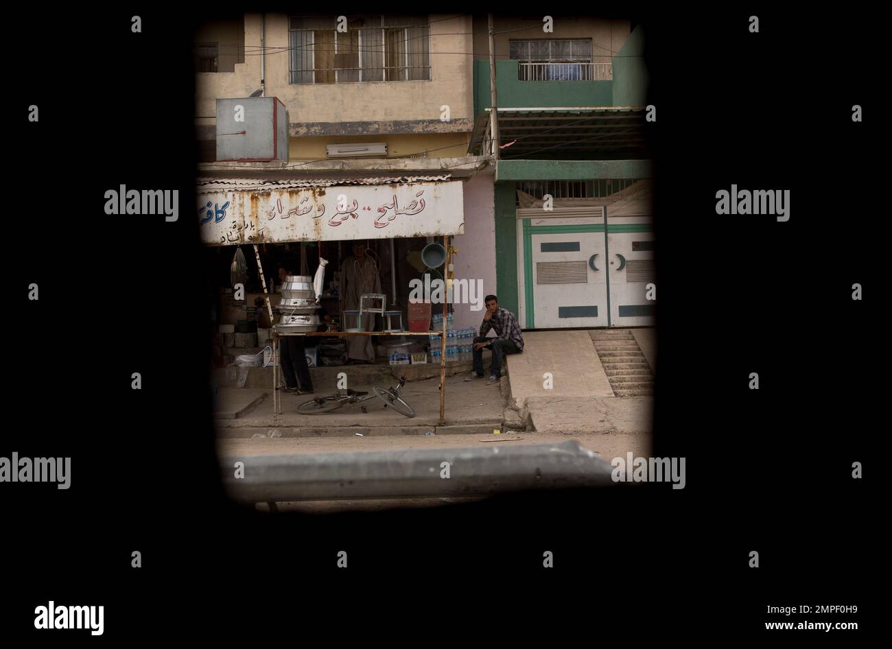 Seen through a Humvee window, a man waits for customers at a small shop ...