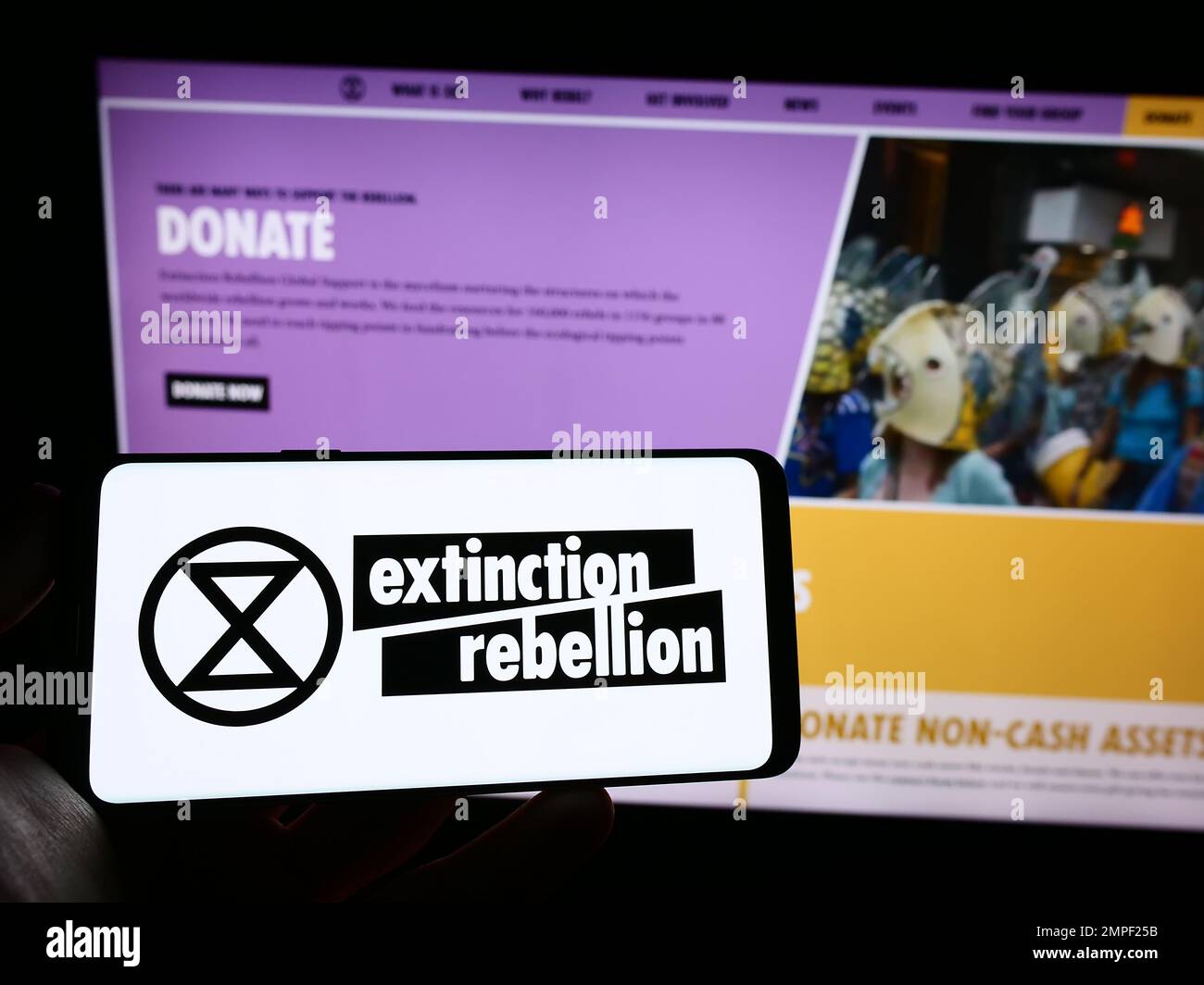 Person holding cellphone with logo of organization Extinction Rebellion (XR) on screen in front of webpage. Focus on phone display. Stock Photo
