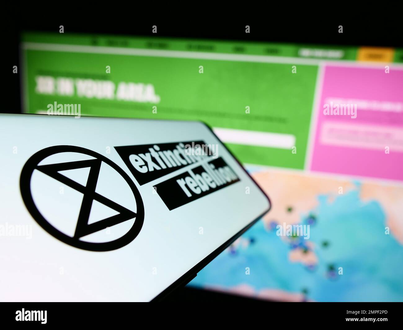 Smartphone with logo of organization Extinction Rebellion (XR) on screen in front of website. Focus on center-left of phone display. Stock Photo