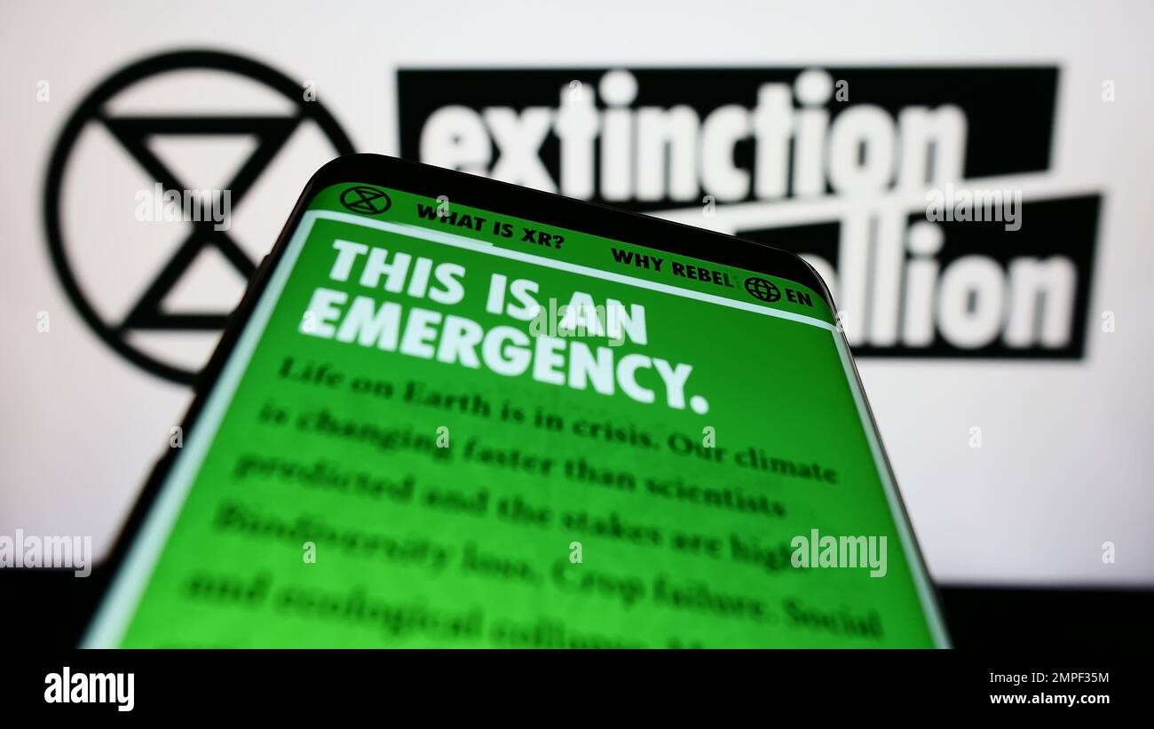 Mobile phone with website of organization Extinction Rebellion (XR) on screen in front of logo. Focus on top-left of phone display. Stock Photo