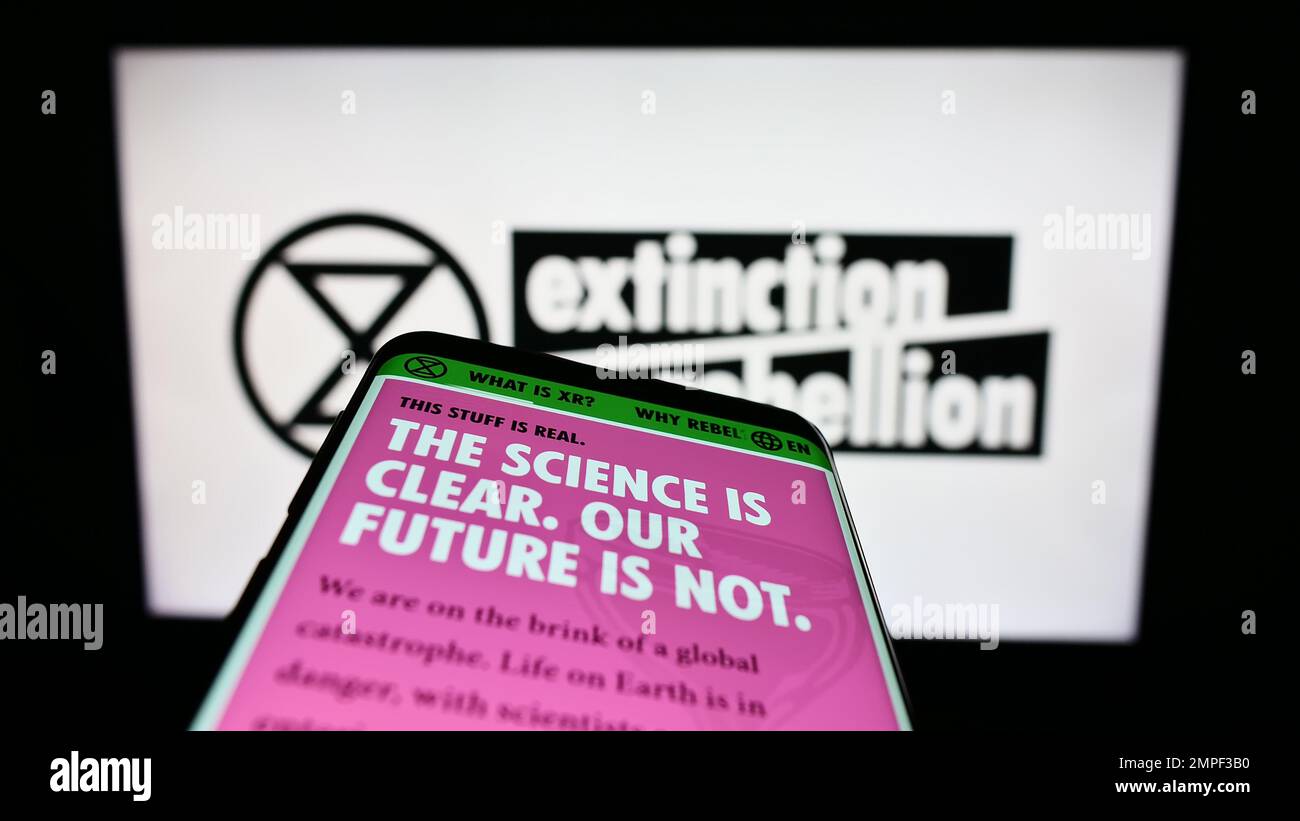 Smartphone with webpage of organization Extinction Rebellion (XR) on screen in front of logo. Focus on top-left of phone display. Stock Photo
