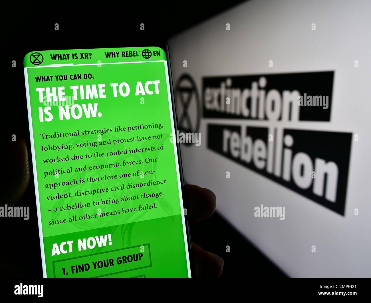 Person holding smartphone with website of organization Extinction Rebellion (XR) on screen in front of logo. Focus on center of phone display. Stock Photo