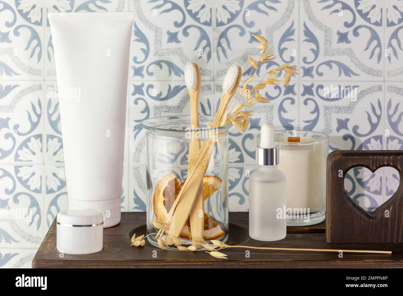 Eco friendly bath still life with bio toothpaste, wooden toothbrushes in a glass jar, organic serum and beauty products on a wooden shelf in bathroom. Stock Photo