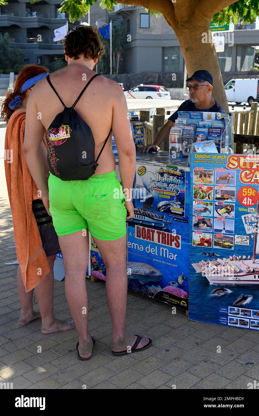 Tourists looking at sales of boating activities offered by street vendor, Maspalomas, Gran Canaria Stock Photo