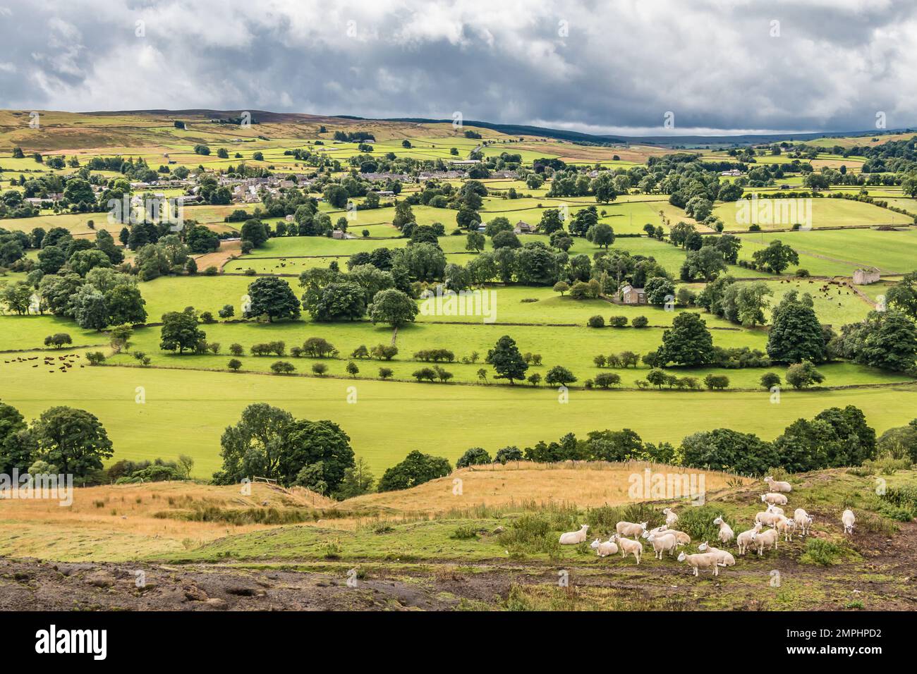 The Teesdale village of Mickleton in strong sunshine during a brief break in the dark cloud cover, as seen from Whistle Crag. Stock Photo