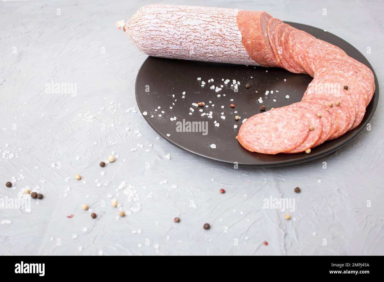 Thin sliced salami on a ceramic black plate, on cement table Stock Photo
